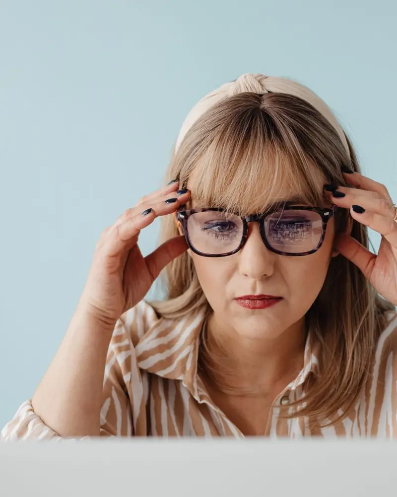 Mulher de óculos ajusta a armação diante da tela do notebook (foto ilustrativa)